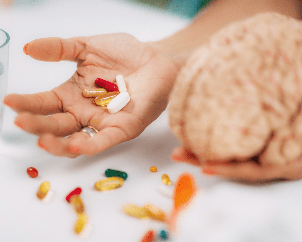 two hands with palms up, one holding a brain model, the other holding different colored pills
